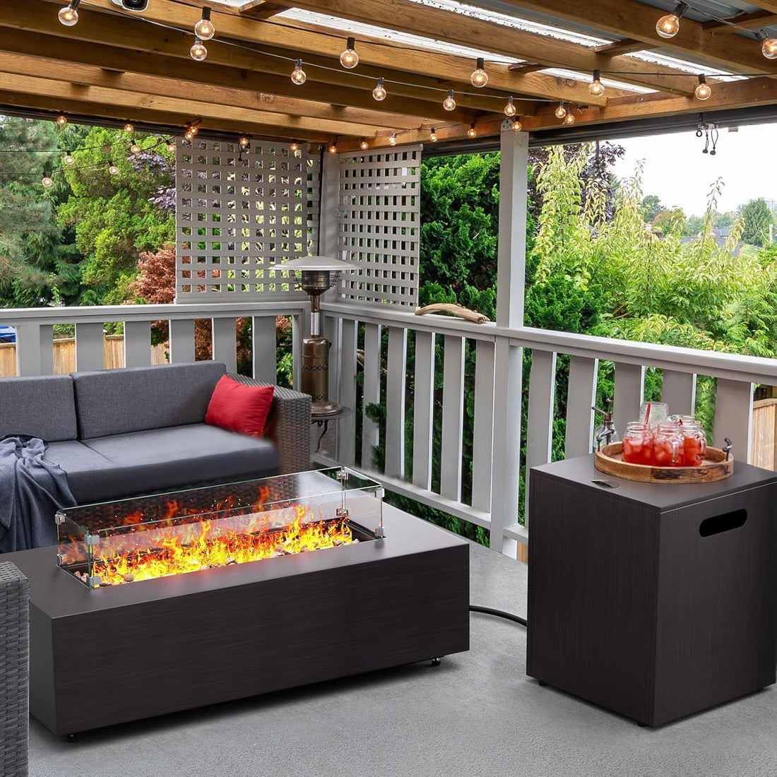 Outdoor patio with fire pit, sofa, and drinks on a deck with greenery in the background