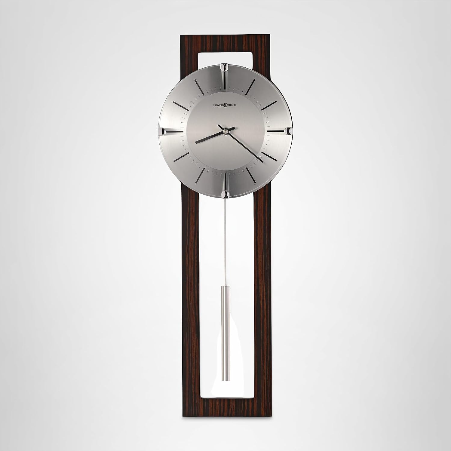 A modern wall clock with a long vertical dark wood-grain frame, a brushed silver round dial with slim black hands and hour markers, and a silver pendulum hanging below, shown against a light gray gradient background.