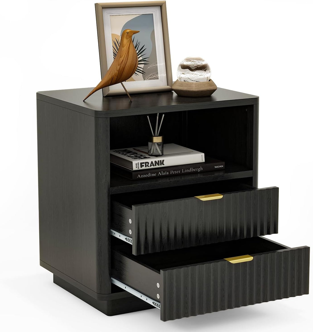A modern black nightstand with two ribbed drawers featuring gold pull handles, shown with one drawer open. The nightstand is styled with a framed bird print, a small decorative object, and books on its top shelf, set against a plain white background.