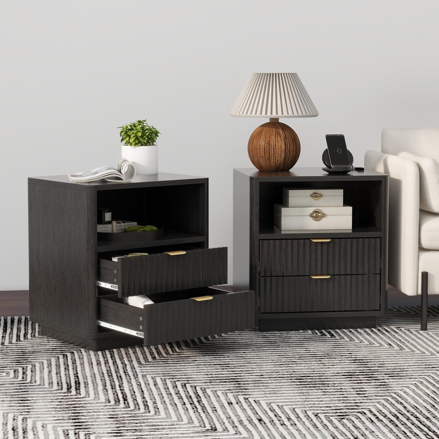 Two modern dark wood nightstands shown in a styled room setting with a patterned rug, a white armchair, and various decorative items on top.