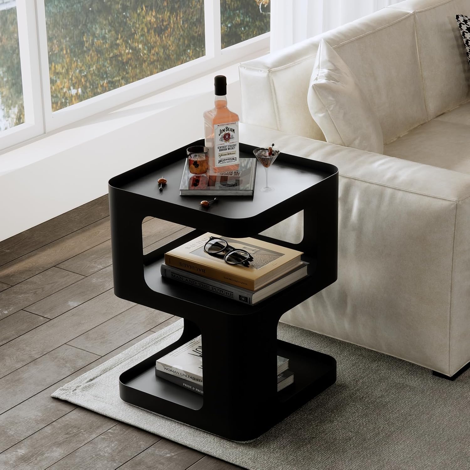 Black side table with books, glasses, and a bottle in a living room setting.