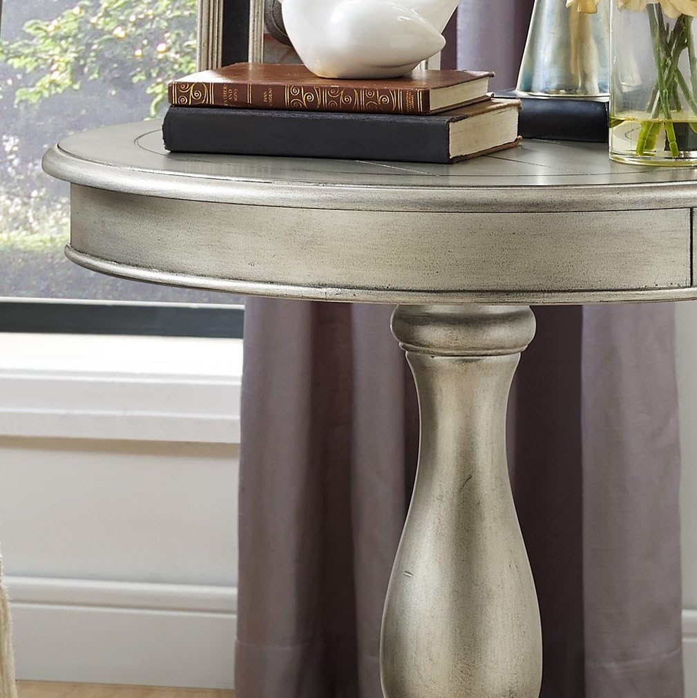 Round metallic table with books and a vase in a room with a window and curtains.