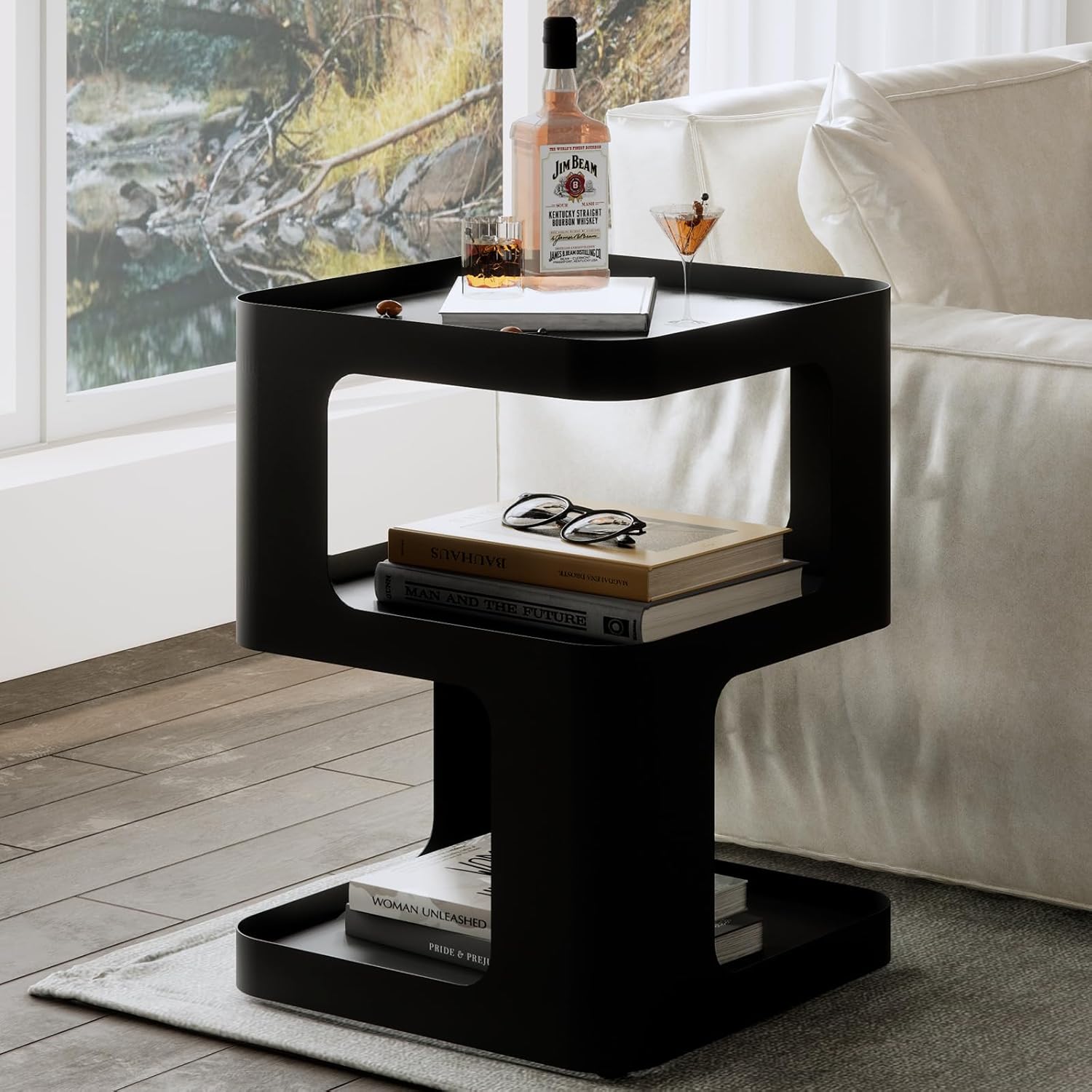 Black side table with books, glasses, and a bottle in a living room setting.
