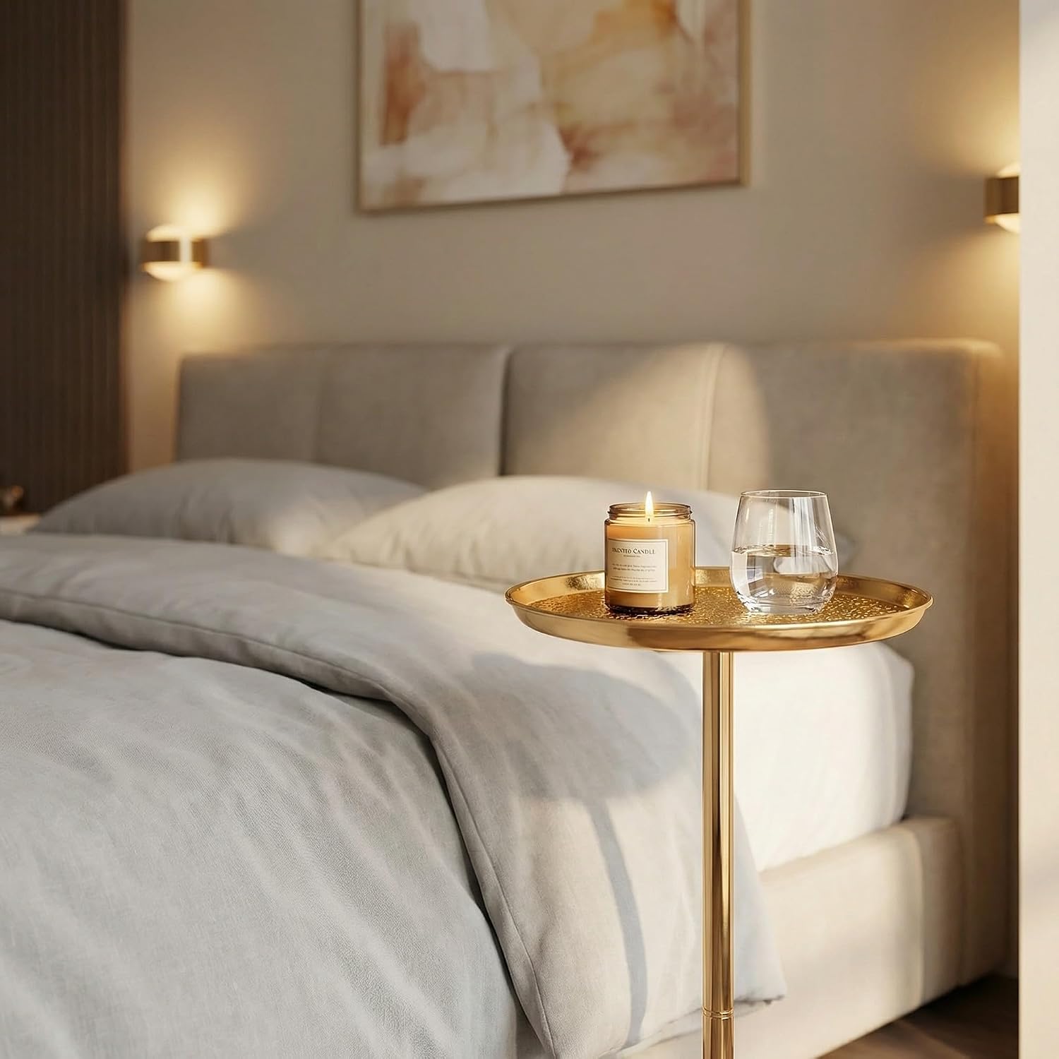 Gold side table with a candle and glass next to a bed in a softly lit bedroom.