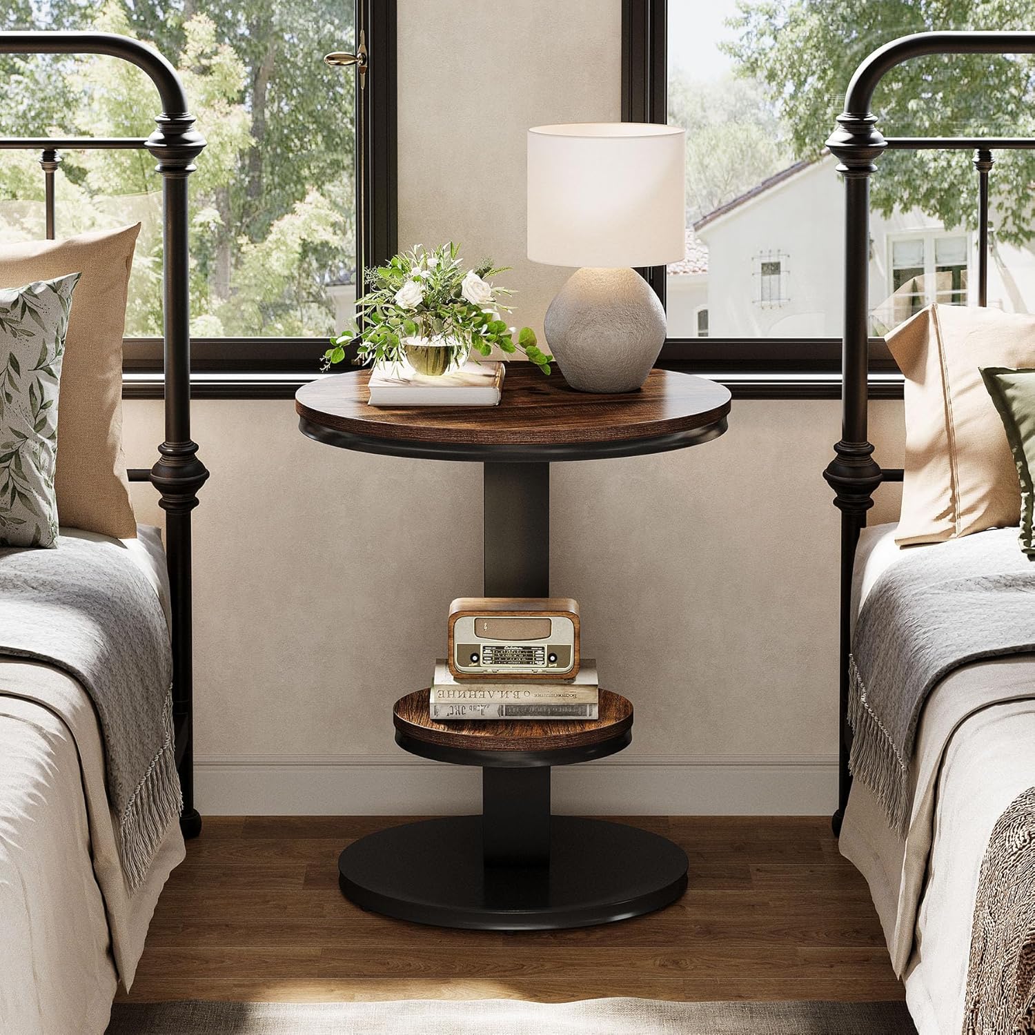 Round wooden side table with decorative items between two beds in a bedroom.