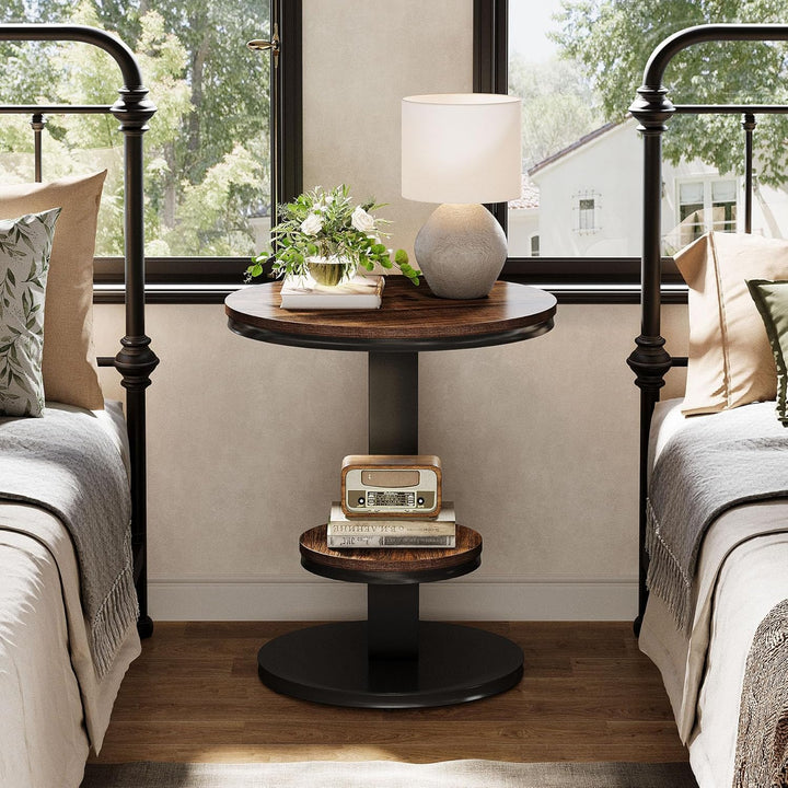 Round wooden side table with decorative items between two beds in a bedroom.