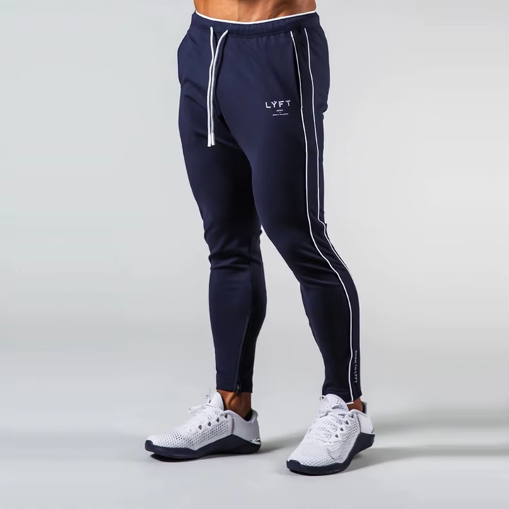 A person wearing navy jogger-style sweatpants with white drawstrings, white side piping, and a small white LYFT logo on the left thigh, paired with white athletic shoes, photographed against a light gray studio background.