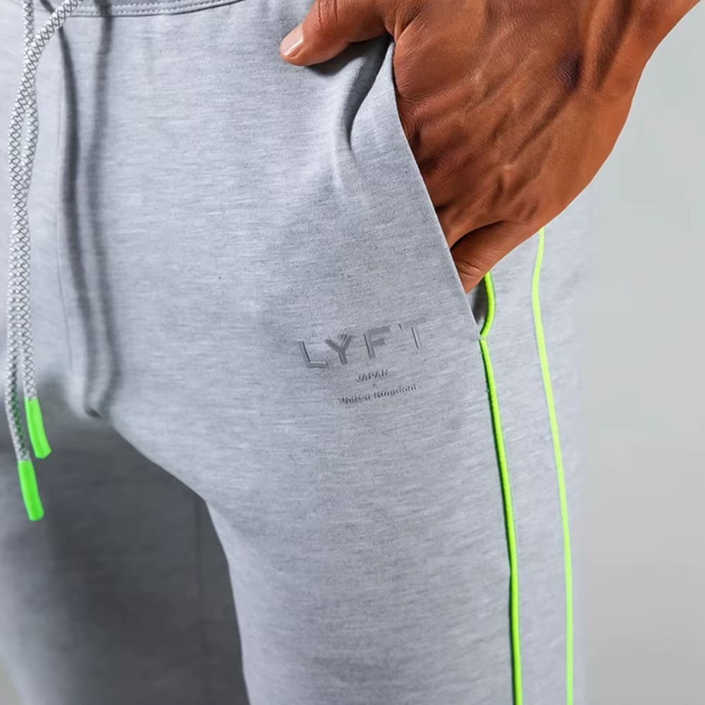 Close-up of a person wearing heather gray sweatpants with a neon green side stripe, a gray drawstring, and a subtle gray LYFT logo on the thigh.