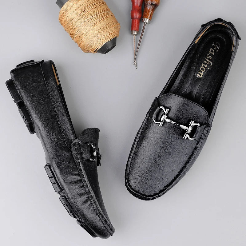 Black loafers with a metallic buckle on a light gray background