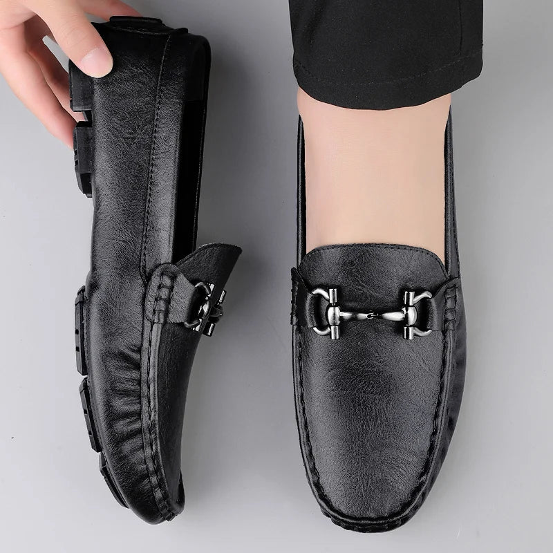 Black loafers with a decorative buckle on a gray background
