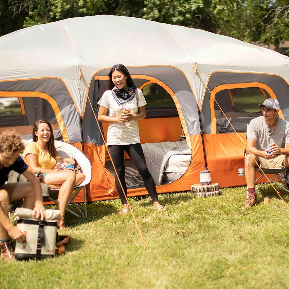 Group of people sitting outside a large camping tent in a grassy area with trees.
