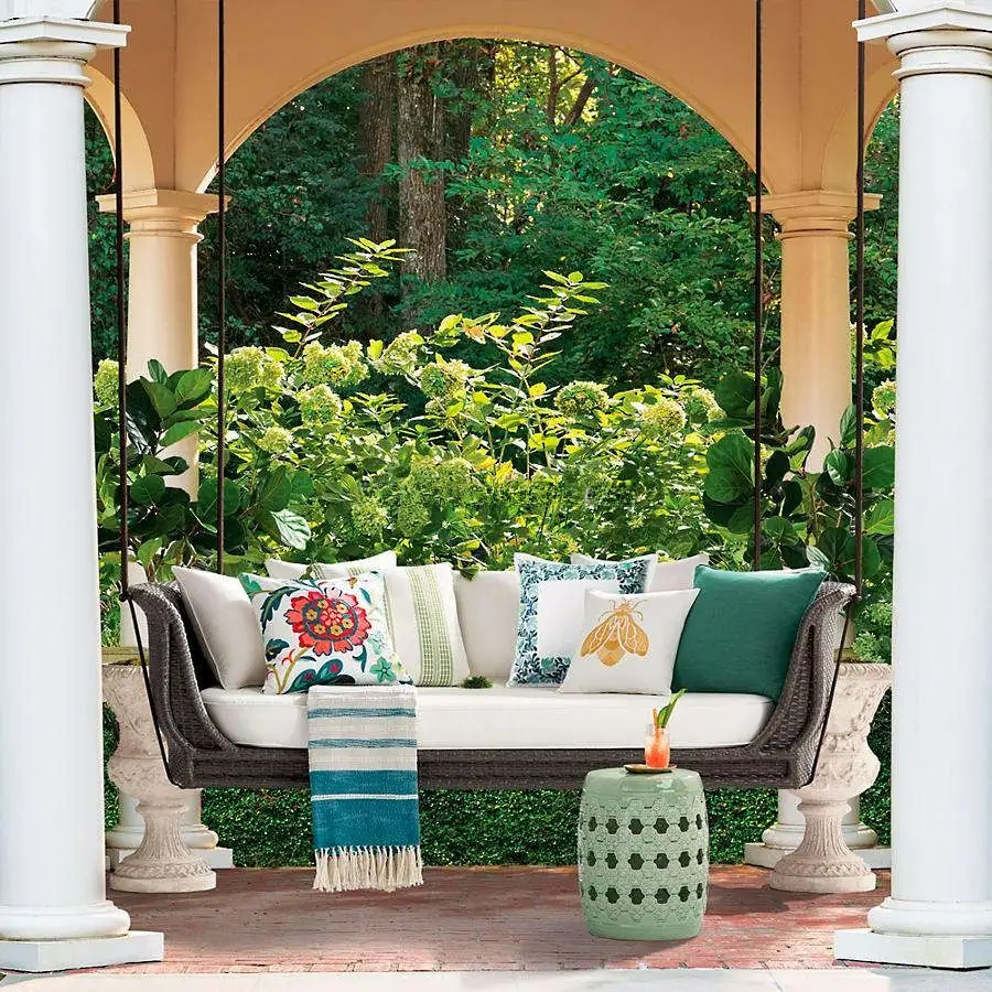 Outdoor swing with colorful cushions and a small table on a patio with columns and greenery.
