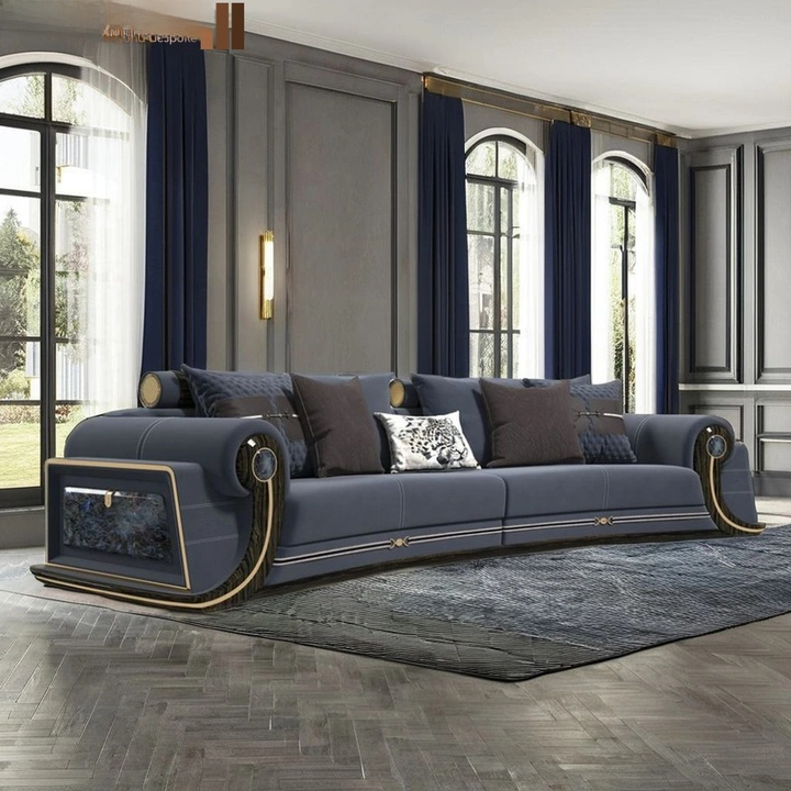 A luxury curved sofa in slate blue with gold trim and dark brown cushions, styled in a grand room with tall windows, navy curtains, and a gray rug.
