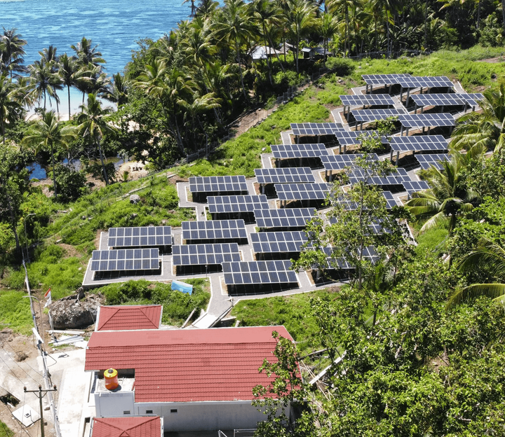 Row of solar panels on a grassy area with a house and ocean in the background