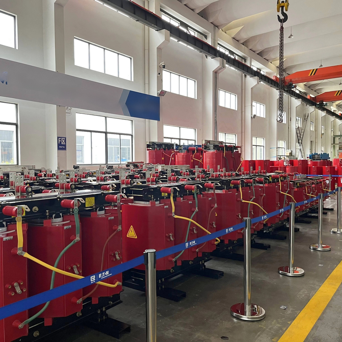 Row of red industrial machines in a large warehouse with high ceilings and large windows.
