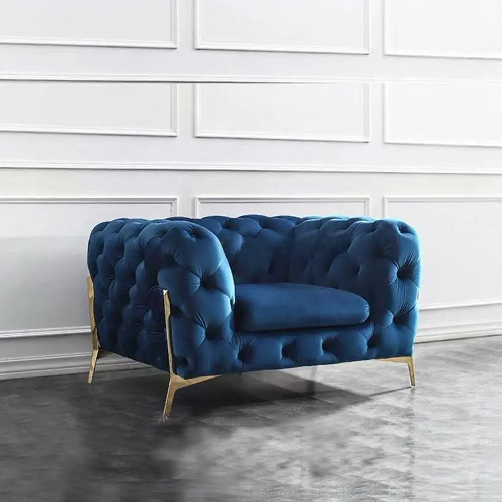 Blue tufted sofa with gold legs in a room with white walls and gray floor.