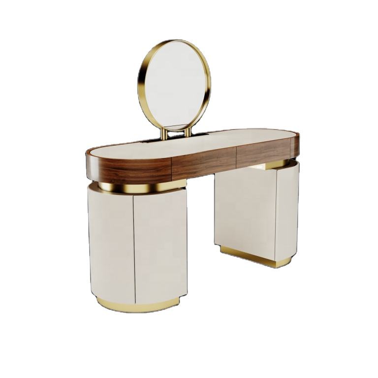 A modern vanity table with an oval mirror, featuring a dark wood top, cream-colored cabinet doors, and polished gold metal accents, isolated on a white background.
