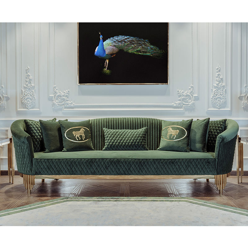 Green velvet sofa with decorative pillows in a room with a peacock painting on the wall.