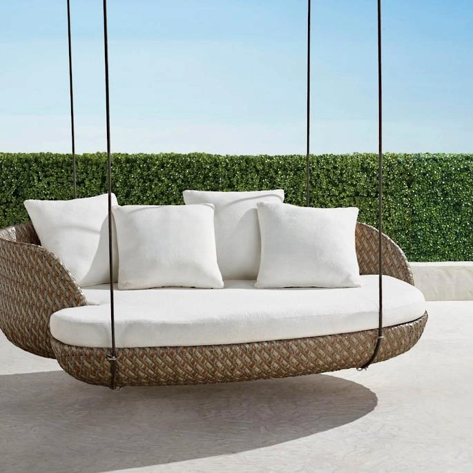 Wicker outdoor swing with white cushions against a clear blue sky and green hedge background