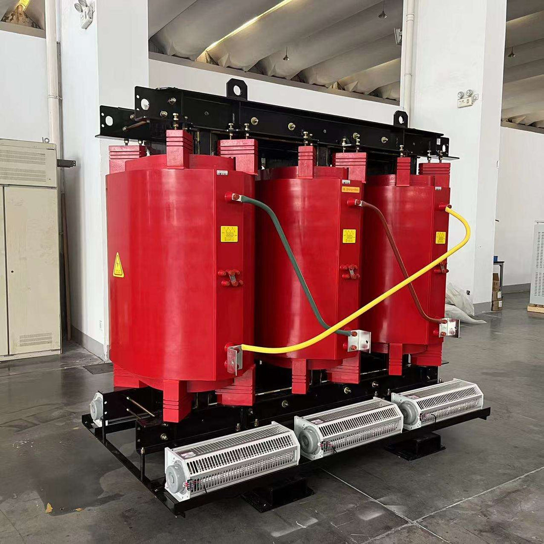 Red transformer with yellow cables in a room with white walls and gray floor.