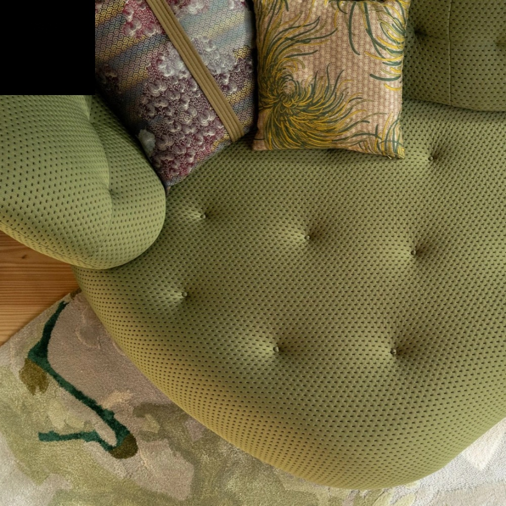 Green tufted chair with patterned cushions on a wooden floor.