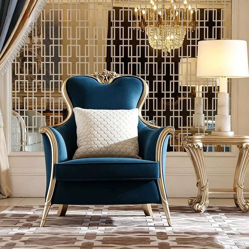 Blue armchair with gold accents in a luxurious room with a chandelier and lamp.