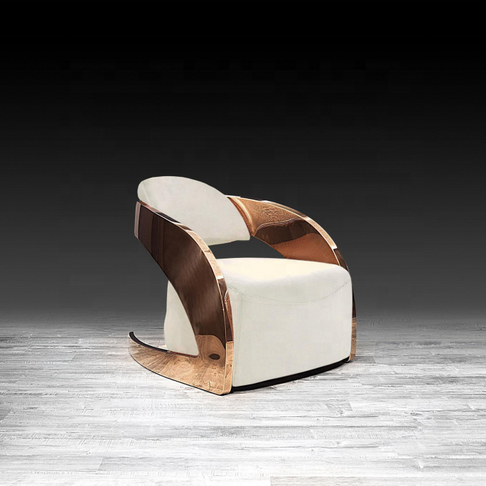 A modern sculptural accent chair with white upholstered seat and back cushions, supported by a curved metallic frame in a polished copper or rose-gold finish, set against a dark gradient studio background and light gray wood floor.