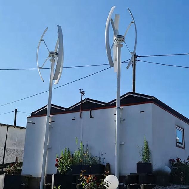 Two wind turbines in front of a building with a clear blue sky.