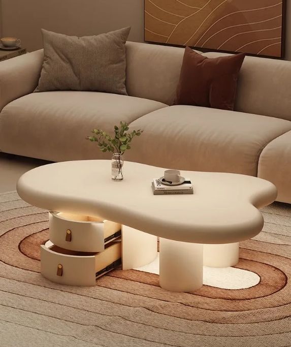 A modern cloud-shaped coffee table with integrated drawers and warm under-table lighting, styled in a cozy living room next to a beige sofa.