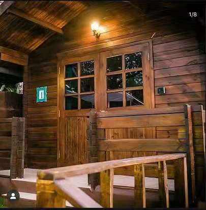 A rustic wooden cabin exterior with a warm glowing wall light, double glass-paneled doors, a wooden bench, and a railing in the foreground.