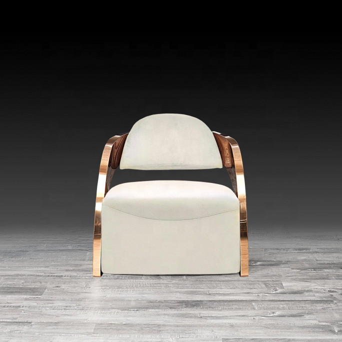 A modern lounge chair with cream-colored velvet upholstery and curved rose gold metal arms and legs, set against a dark gray gradient background with a gray wood floor.