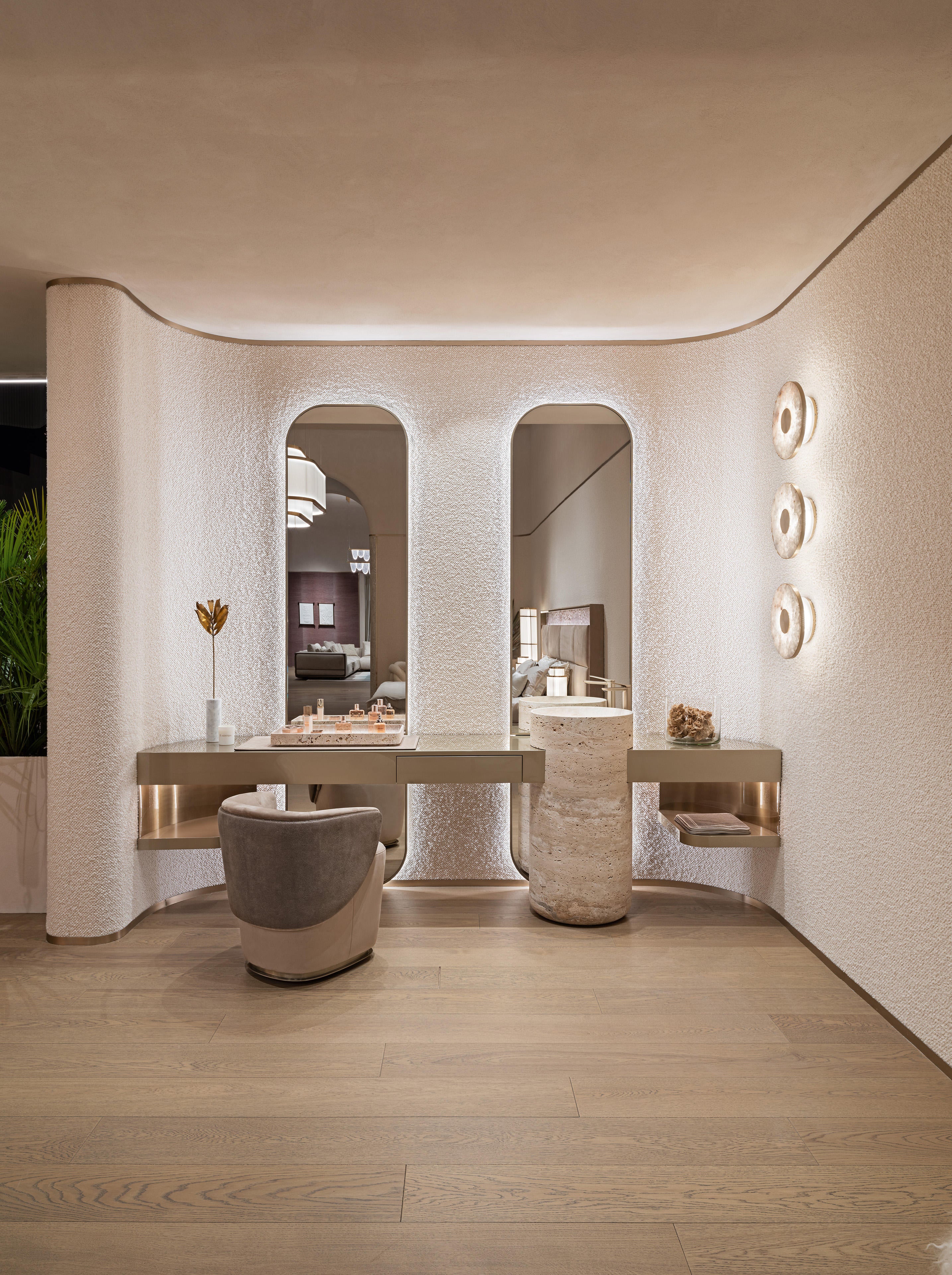 A luxury modern vanity area with a long floating desk, two arched mirrors, a textured gray and beige accent chair, and warm ambient lighting on a light wood floor.