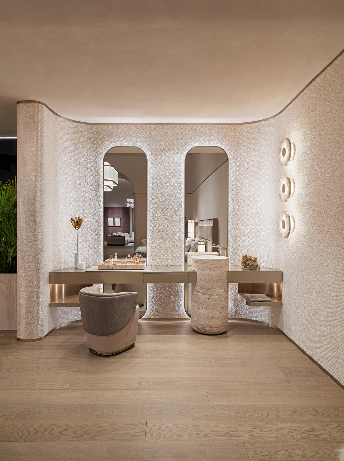 A luxury modern vanity area with a long floating desk, two arched mirrors, a textured gray and beige accent chair, and warm ambient lighting on a light wood floor.