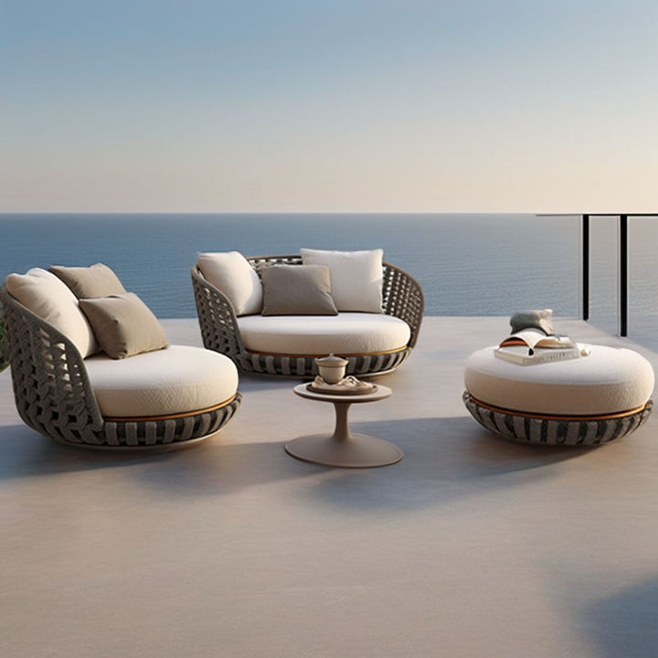 Outdoor furniture set with chairs, ottoman, and table on a deck with ocean view.