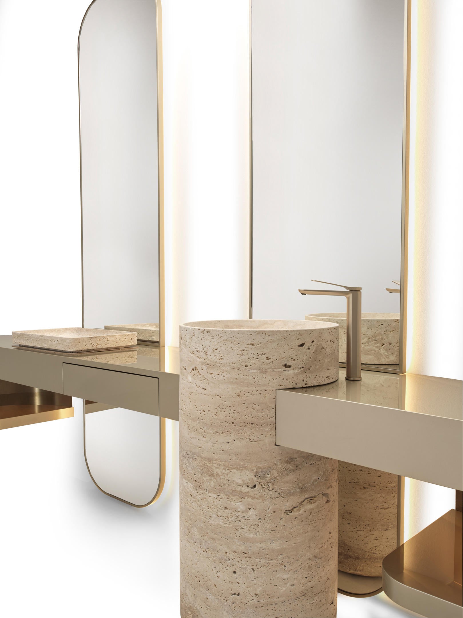 Modern vanity setup with cylindrical stone pedestal sinks, a matching stone soap dish, and sleek metallic faucets in front of large wall mirrors with warm lighting.