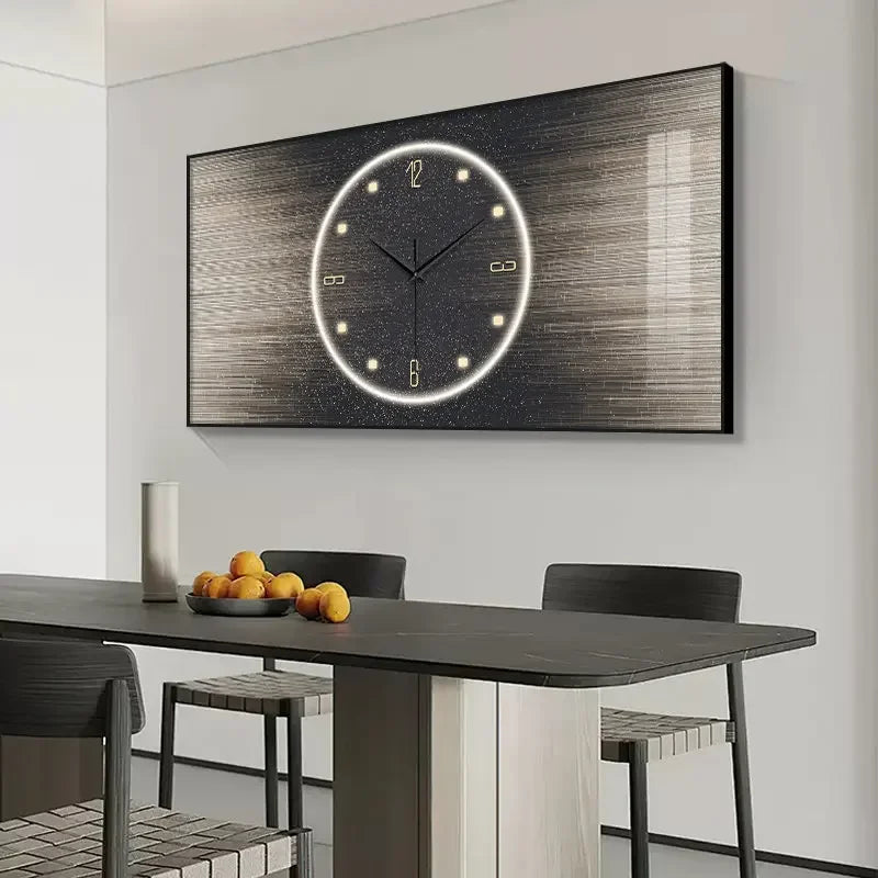 A large rectangular wall clock with a dark textured background and a glowing circular white clock face, mounted on a light gray wall above a dining table with chairs and fruit.