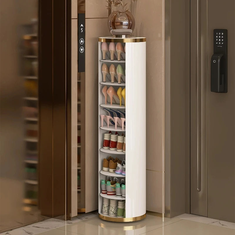 A tall, slim cylindrical shoe rack with a white body and gold trim, filled with various shoes, positioned in a modern entryway next to an elevator and door.