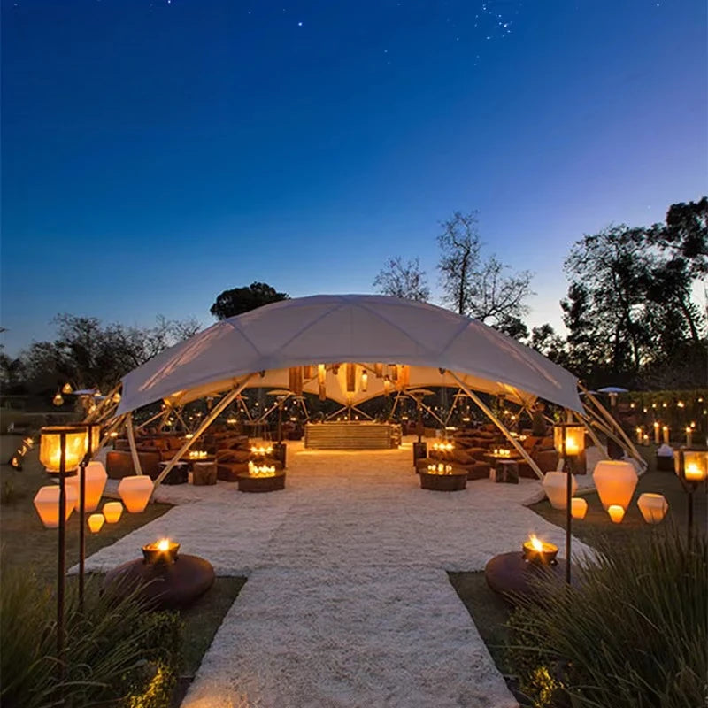 Outdoor event setup with a large white tent illuminated by candles and lanterns at night.