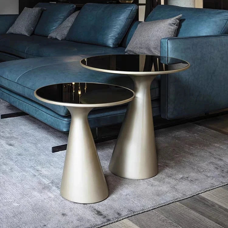 Two metallic side tables in front of a blue leather sofa.