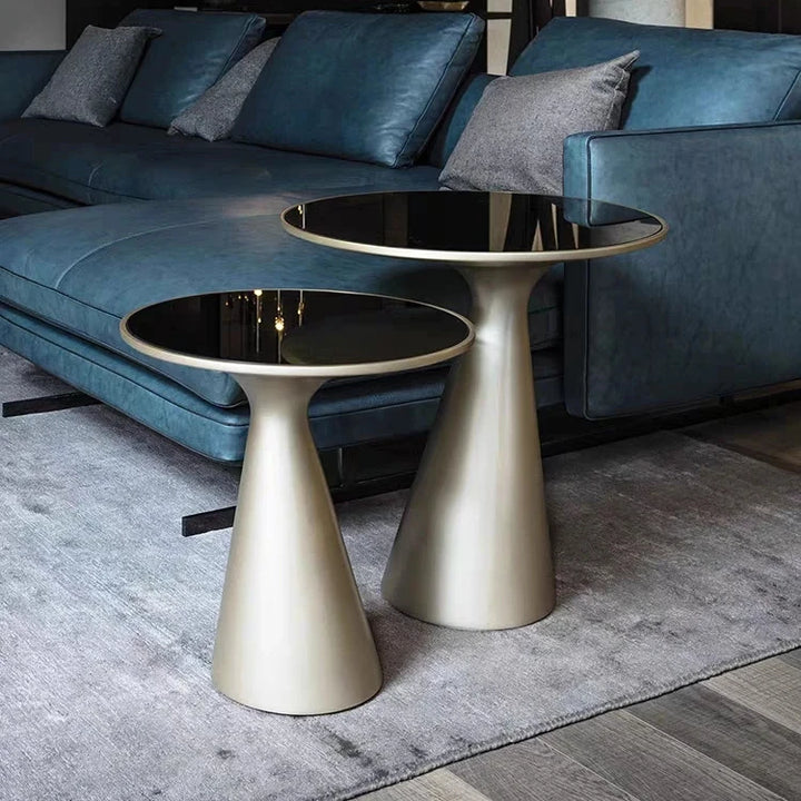 Two metallic side tables in front of a blue leather sofa.