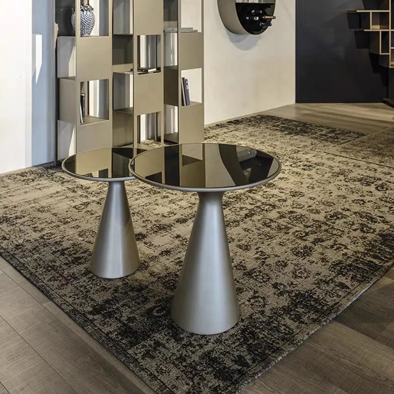 Modern glass table with metallic base on a patterned rug in a stylish room.