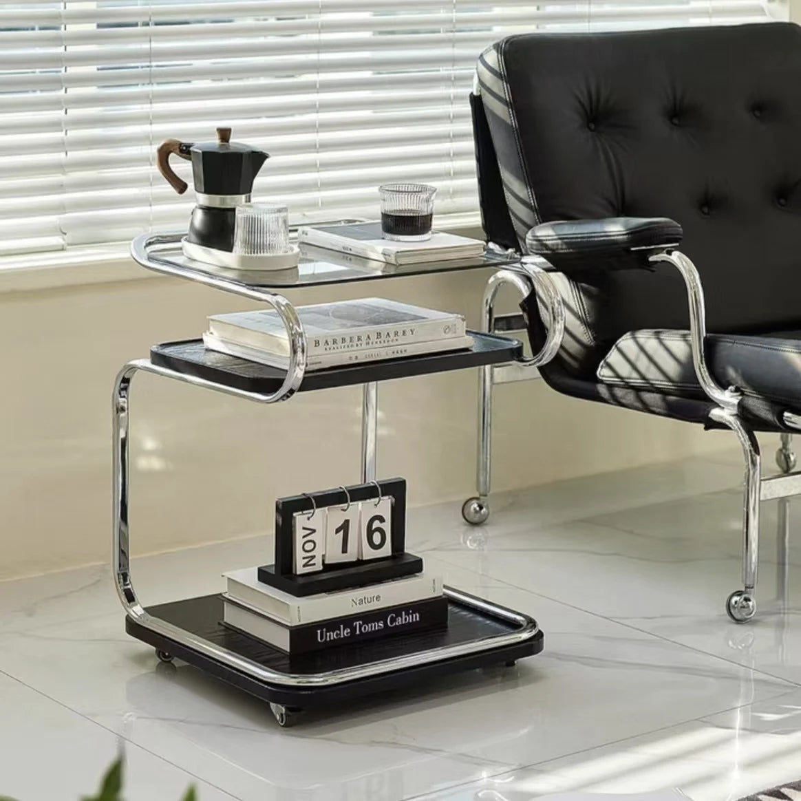 Modern black and glass side table with books and a calendar next to a black chair.