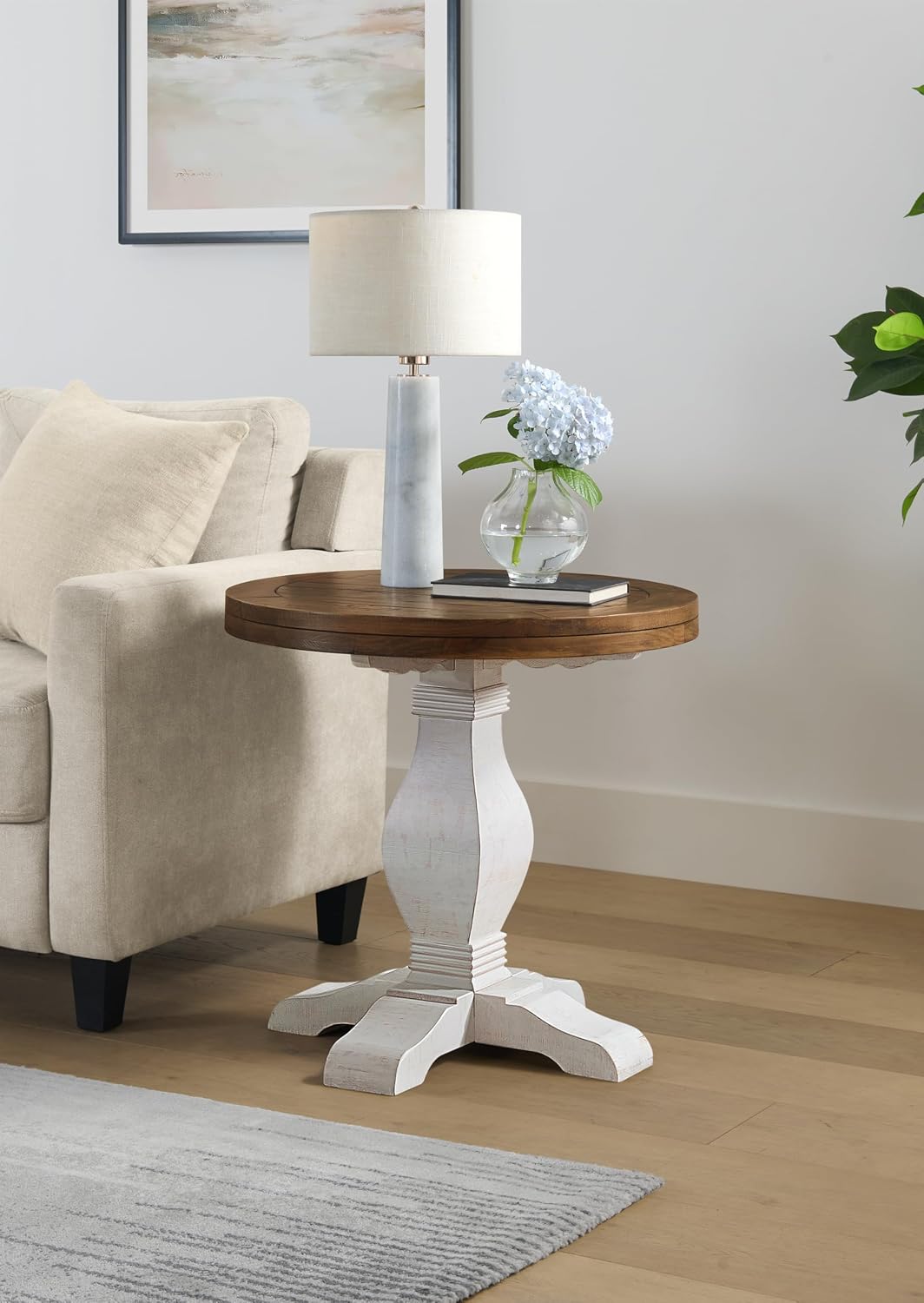 Round wooden side table with white base in a living room setting.