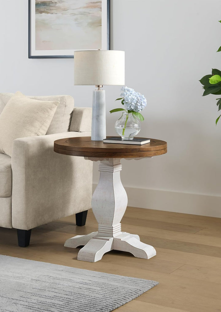 Round wooden side table with white base in a living room setting.
