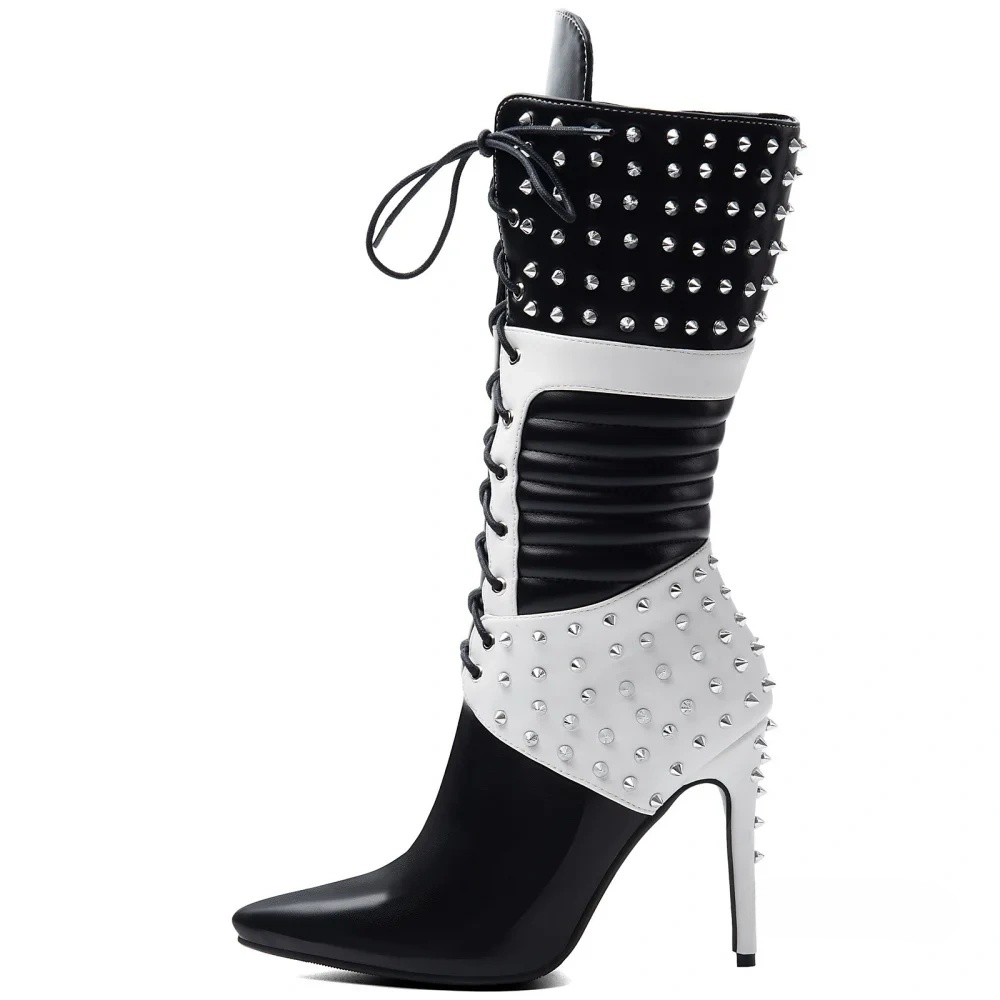 A knee-high studded boot with a pointed toe and high stiletto heel, featuring a black and white color-blocked design with silver-tone studs and side laces, shown against a plain white background.