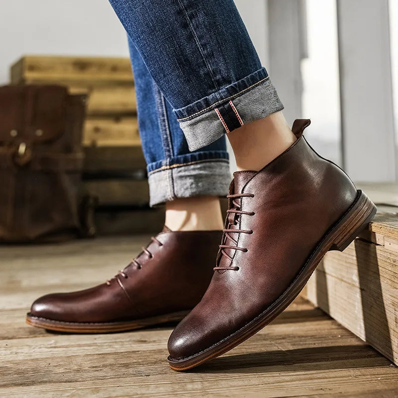 Brown leather shoes worn with rolled-up jeans on a wooden floor.