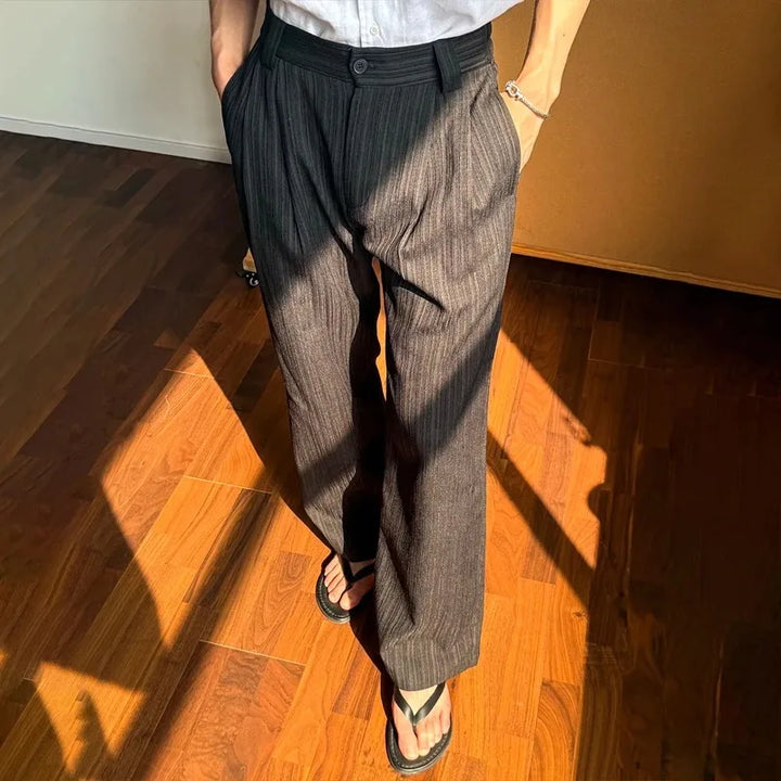 Person wearing brown pinstripe pants and a white shirt on a wooden floor.