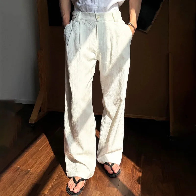 Person wearing light-colored wide-leg pants standing indoors with wooden flooring.