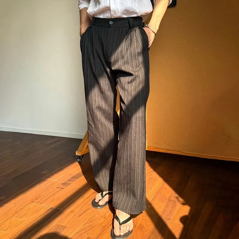 Person wearing brown striped pants and a white shirt in a room with wooden floor and orange wall.